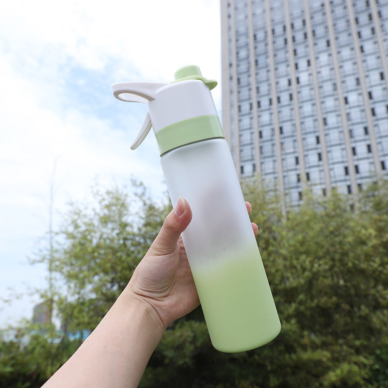 Hand holding a gradient green and white water bottle with a building in the background