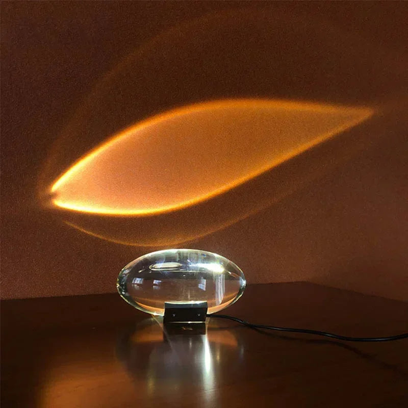 Modern table lamp with a clear glass shade casting a warm glow on a dark surface.