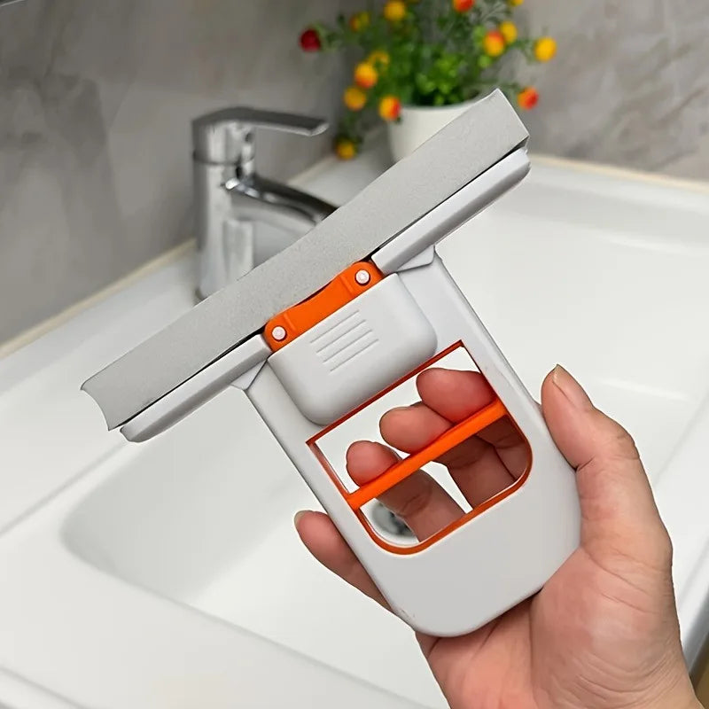 Hand holding a white and orange window cleaning tool with a sink and flowers in the background