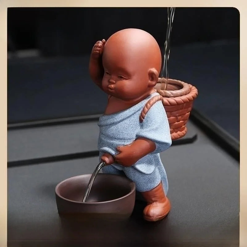 Ceramic figure of a monk pouring water from a pot into a bowl on a dark surface.