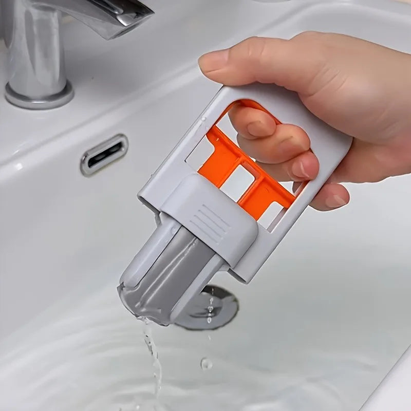 Hand holding a gray and orange cleaning tool over a sink with water flowing.