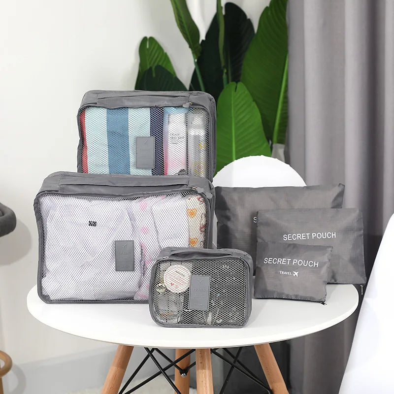 Set of gray packing cubes with items on a white table, plants in the background