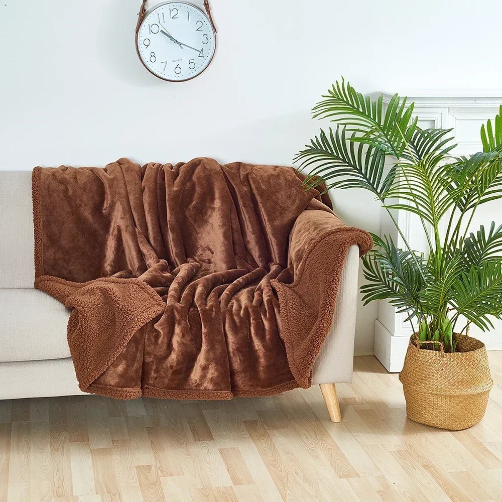 Brown blanket draped over a white sofa in a room with a clock on the wall and a plant.