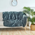 Blue blanket draped over a beige sofa in a living room with a clock and plant in the background.