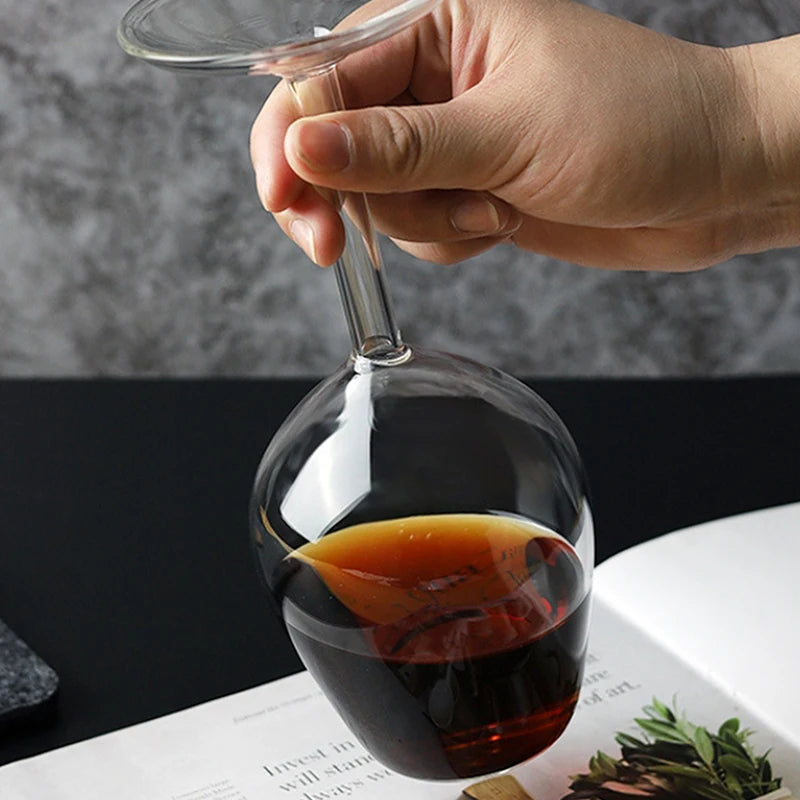 Hand holding a glass with dark liquid and an orange slice, placed on a magazine.