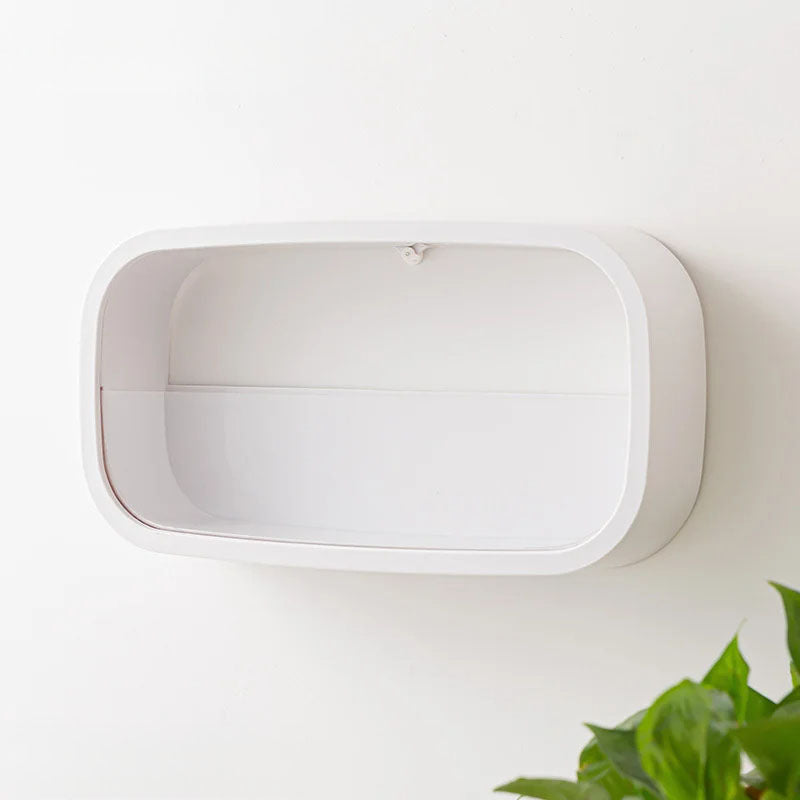 White wall-mounted device on a light gray background with a plant in the corner.