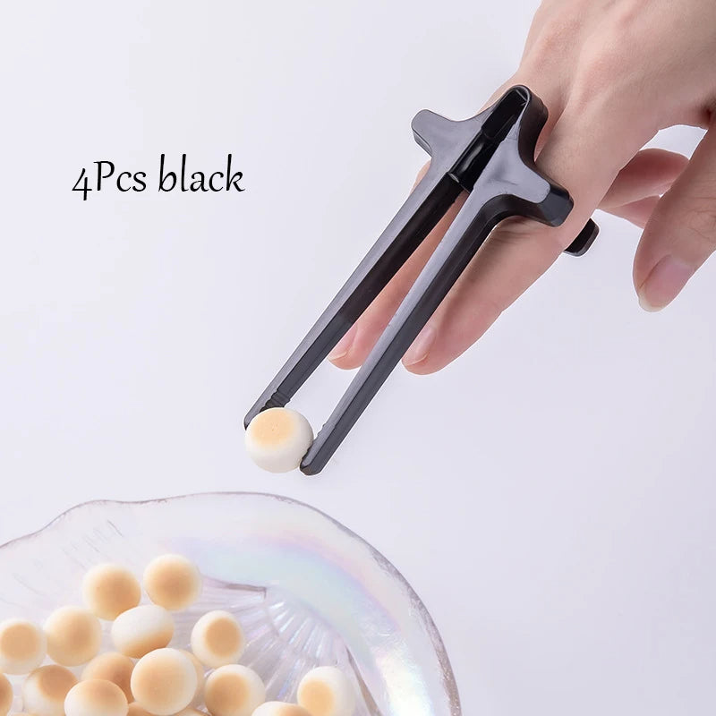 Hand using black tongs to pick up a ball from a clear container on a white background