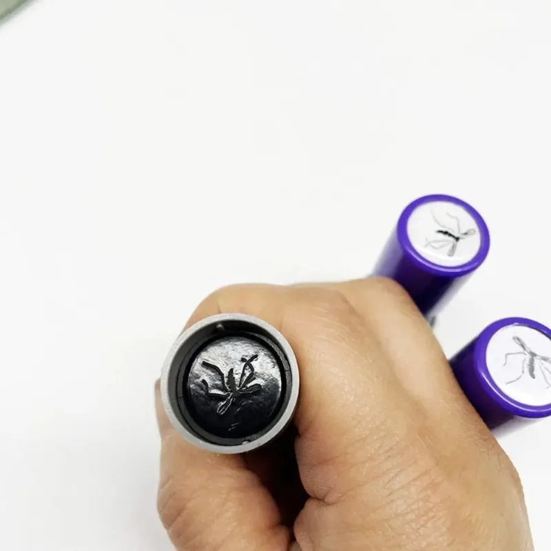 Hand holding a black and silver stamp with purple stamps in the background on a white background