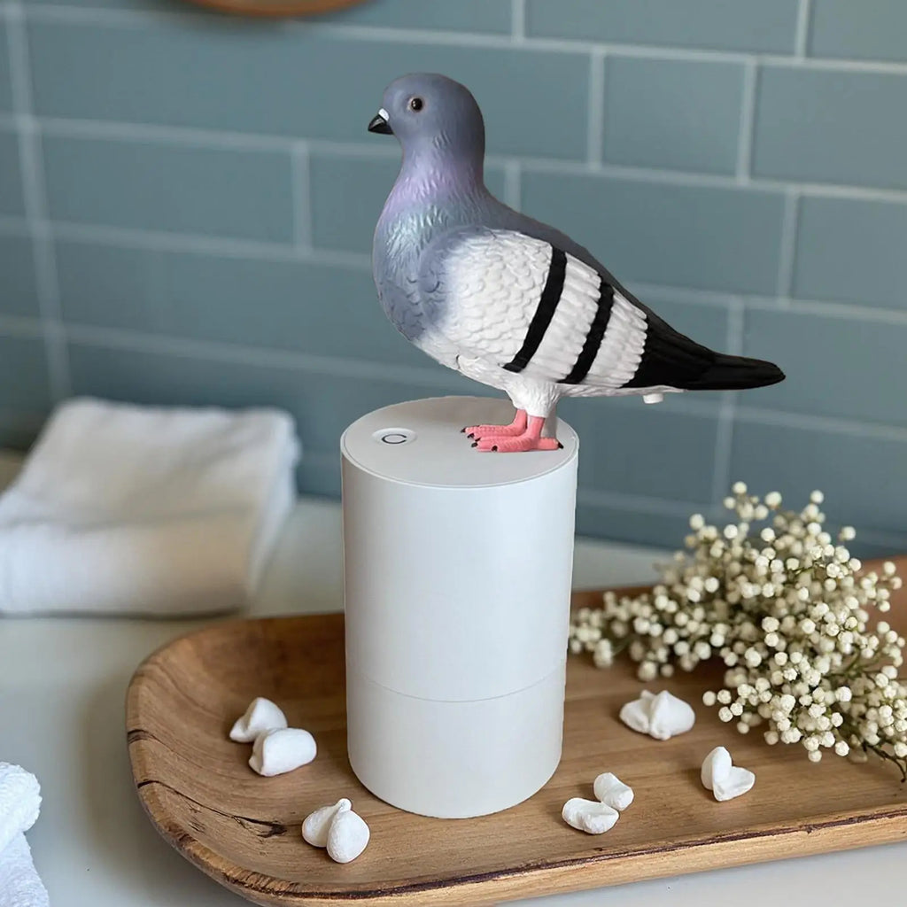 Pigeon-shaped diffuser on a white cylindrical base with flowers and cotton balls on a wooden tray.