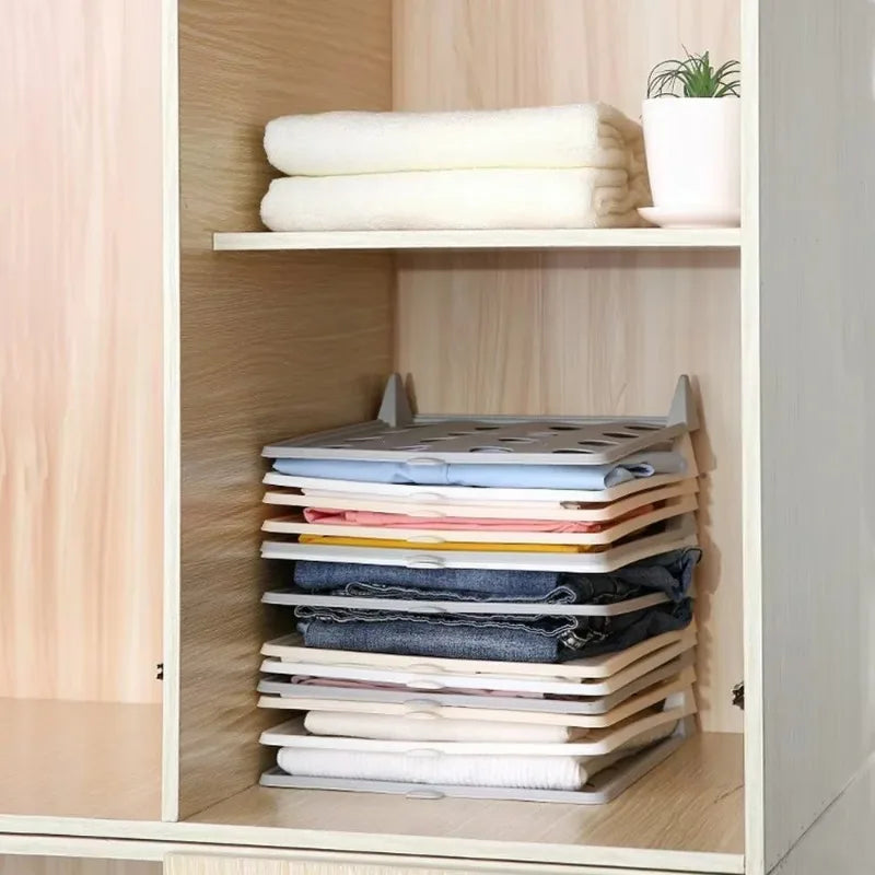 Stack of folded clothes on a wooden shelf with a plant in the background